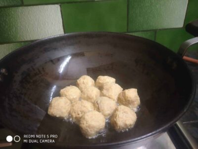 Golden fried snack balls cooking in a black frying pan on a stovetop.