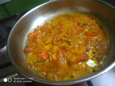 Fiery tomato and onion curry cooking in a stainless steel pan for delicious food recipes.