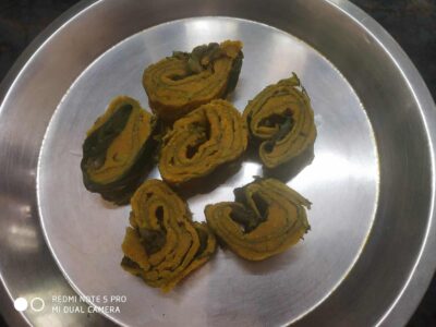 Golden Indian baingan (Eggplant) rolls with spices on a stainless steel plate.
