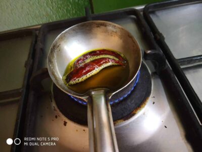 Sizzling dried red chili peppers in hot oil on stove for spicy cooking.