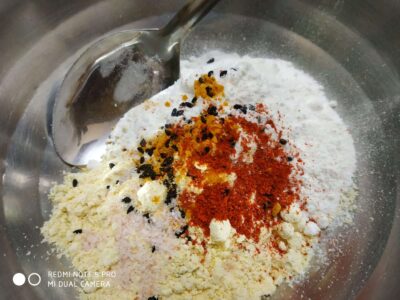 Chickpea flour mixture with spices in a stainless steel bowl for Indian snack preparation.