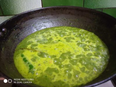 Creamy green chutney cooking in a black skillet, vibrant and flavorful Indian condiment.
