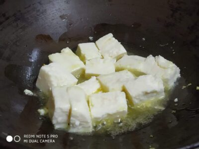 Creamy paneer cubes being cooked in a hot skillet for flavorful Indian dish preparation.