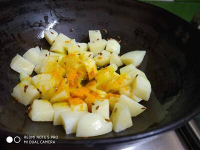 Sweet potatoes cooking with turmeric and cumin seeds in a black skillet for a delicious recipe.