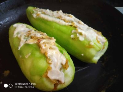 Stuffed green bell peppers with cheese and herbs on a black baking tray.