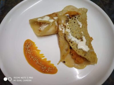 Golden fried paneer stuffed paratha with creamy dipping sauce and a drizzle of orange chutney, served on a white plate.