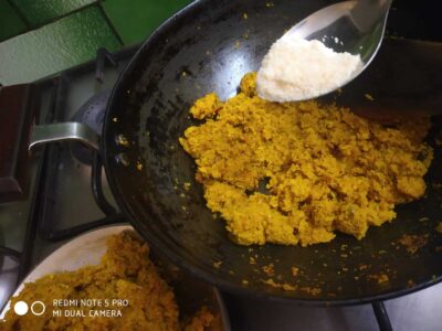 Bright yellow mashed pumpkin being cooked in a pan with added grated cheese, ready for delicious pumpkin cheese mash.