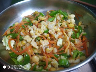 Colorful vegetable stir-fry with carrots, cauliflower, corn, and green peppers in a stainless steel pan.