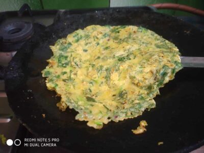 Golden vegetable omelette cooking on a black pan with herbs and vegetables.