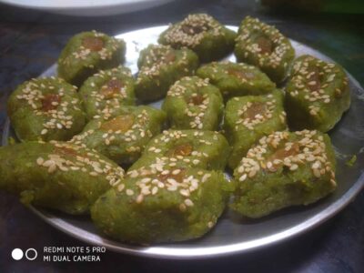 Fresh green jaggery and sesame ladoos on a silver plate, traditional Indian sweet delicacies.
