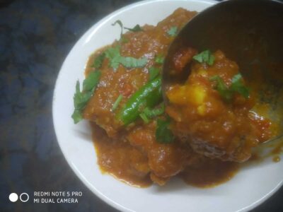 Spicy fish curry garnished with cilantro on a white plate, served with a green chili pepper.